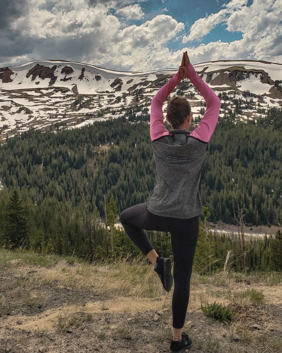 Heather in tree pose facing snow-dusted mountains and evergreen forest